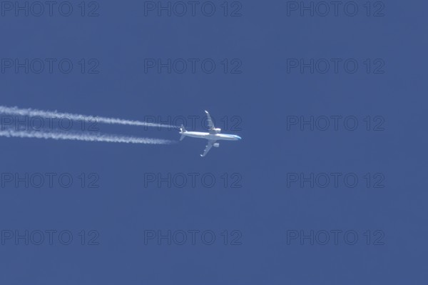 Jet passenger aircraft flying in a blue sky with contrails or vapour trails behind, England, United Kingdom