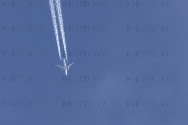 Boeing 777 jet passenger aircraft of Qatar airways airlines flying in a blue sky with contrails or vapour trails behind, England, United Kingdom