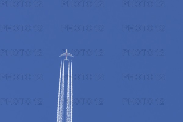 Airbus A380 jet passenger aircraft of Emirates airlines flying in a blue sky with contrails or vapour trails behind, England, United Kingdom