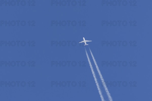 Jet passenger aircraft flying in a blue sky with contrails or vapour trails behind, England, United Kingdom