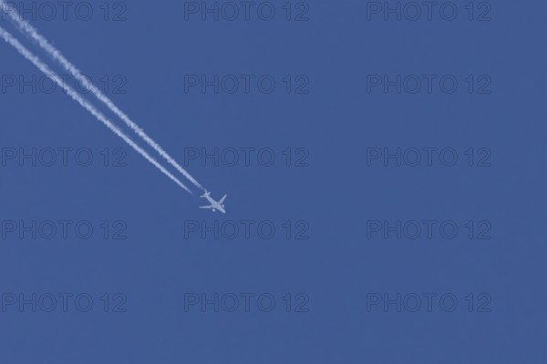 Airbus jet passenger aircraft flying in a blue sky with contrails or vapour trails behind, England, United Kingdom