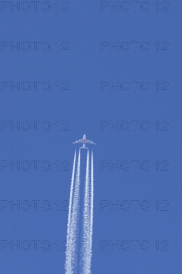 Airbus A380 jet passenger aircraft of Emirates airlines flying in a blue sky with contrails or vapour trails behind, England, United Kingdom