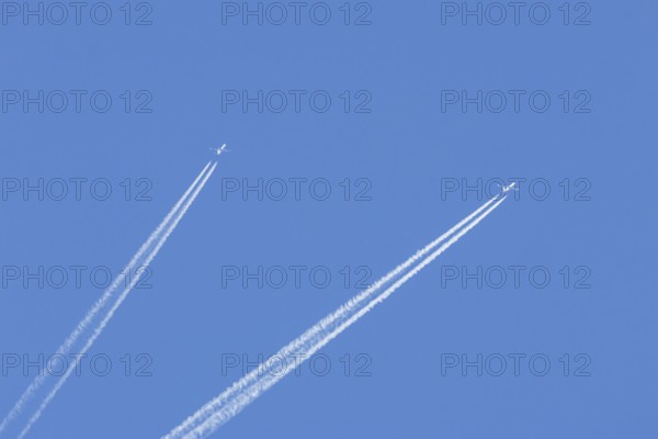 Two jet passenger aircraft flying in a blue sky with contrails or vapour trails behind, England, United Kingdom