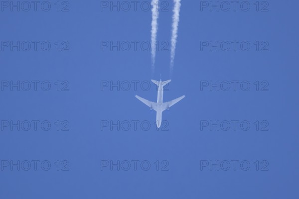 Jet passenger aircraft flying in a blue sky with contrails or vapour trails behind, England, United Kingdom