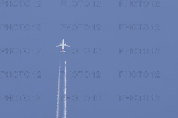 Airbus jet passenger aircraft flying in a blue sky with contrails or vapour trails behind, England, United Kingdom