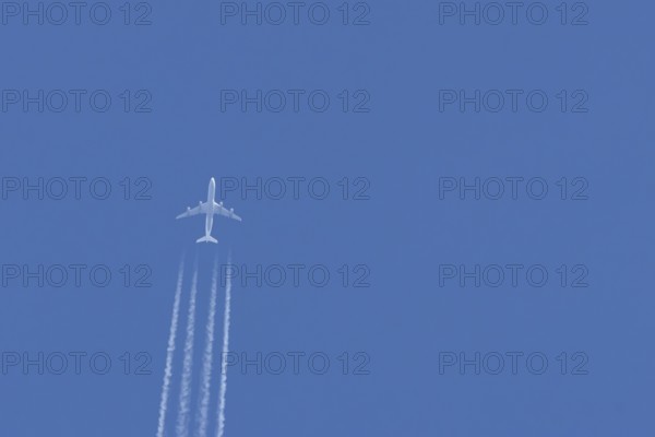 Jet passenger airliner aircraft flying in a blue sky with contrails or vapour trails behind, England, United Kingdom