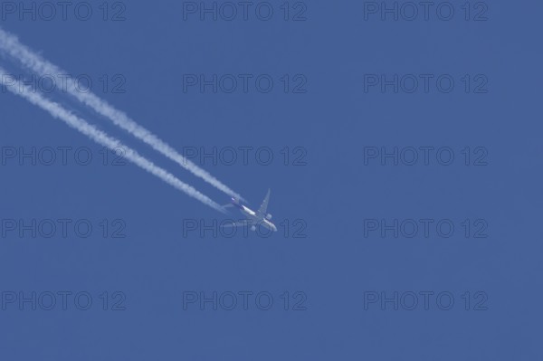 Boeing 777 jet cargo aircraft of FedEx Express airlines flying in a blue sky with contrails or vapour trails behind, England, United Kingdom