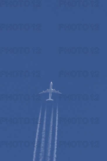 Jet commercial passenger aircraft flying in a blue sky with contrails or vapour trails behind, England, United Kingdom
