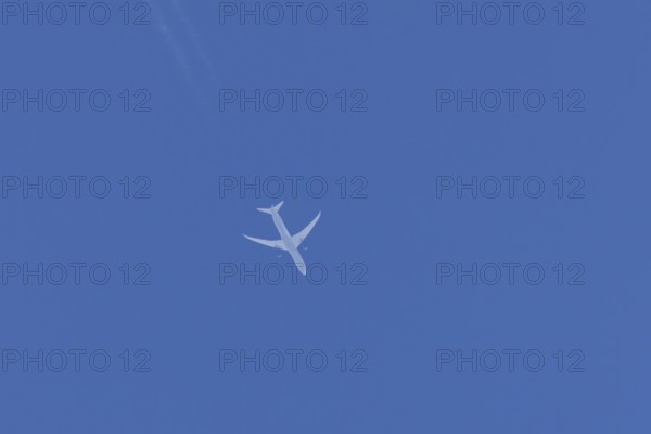 Boeing jet passenger aircraft flying in a blue sky with contrails or vapour trails behind, England, United Kingdom