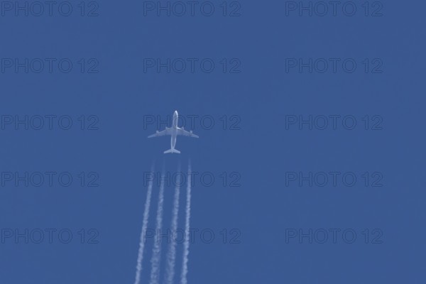 Jet commercial passenger aircraft flying in a blue sky with contrails or vapour trails behind, England, United Kingdom