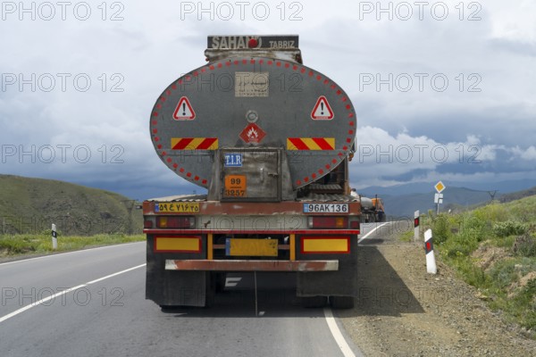 A truck drives on a winding road through a mountainous landscape under cloudy sky, truck with Iranian license plate, Syunik province, Armenia