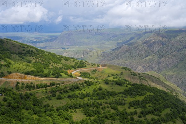 Wide green landscape with hills and a winding road under cloudy sky, landscape near Ltsen, Syunik province, Syunik, Caucasus, Armenia