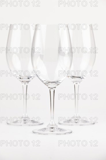 Three elegant, transparent wine glasses with long stems against a neutral background