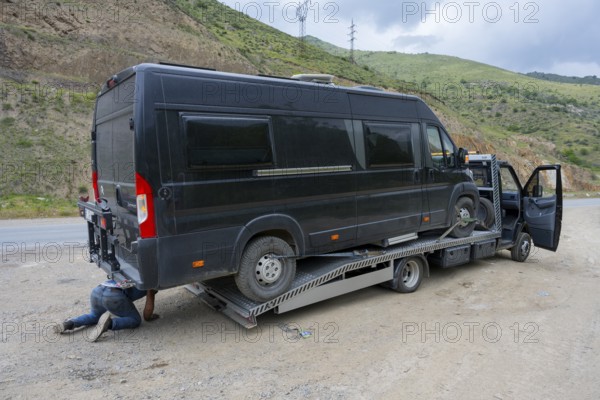 Black van on a car transporter, driver working under the vehicle, camper being towed, motorhome, Lernadzor, Syunik province, Caucasus, Armenia