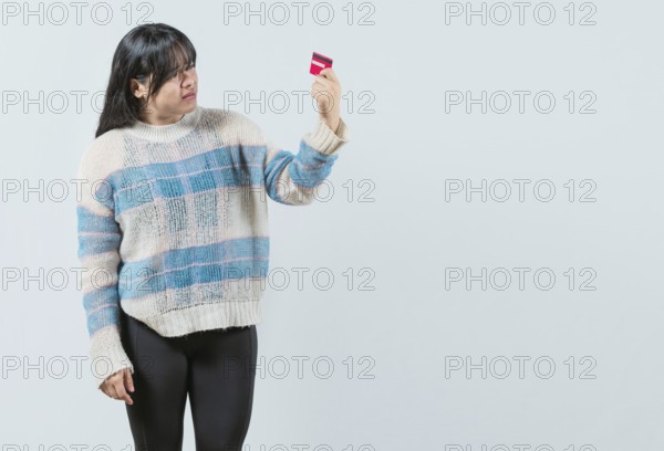 Unsure and confused young woman holding and looking at a credit card isolated. Confused asian girl holding a debit card