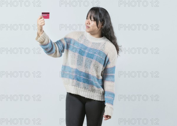 Confused asian girl holding a credit card isolated. Unsure and confused young woman holding and looking at a credit card