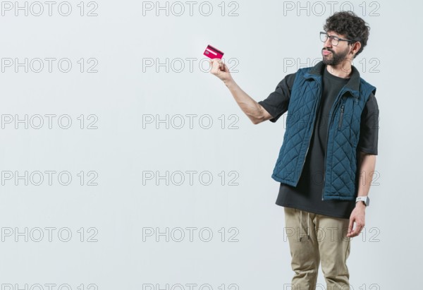Confused modern guy holding a credit card isolated. Unsure and confused young man holding and looking at a credit card