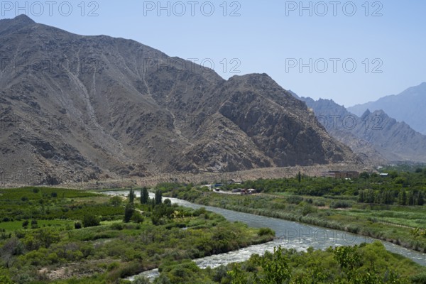 A river flows through a lush green landscape against a mountain backdrop, view of Iran, Aras River near Meghri, Syunik Province, Syunik, Armenia