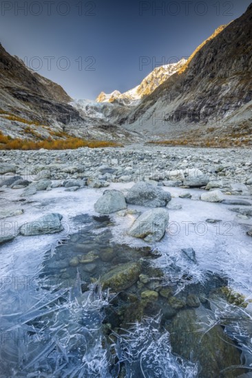 Ice structures on mountain stream with autumnal larches and mountain panorama, Ferpecle glacier, Val d'Herens, Canton of Valais, Switzerland