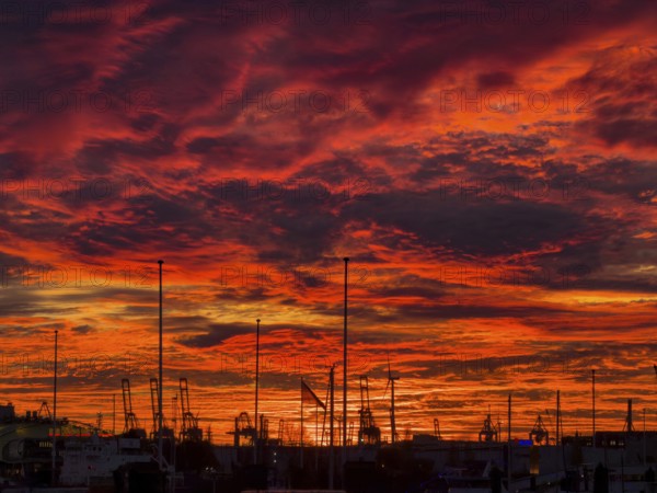 Dramatic sunset sky at Hamburg's Landungsbrücken with silhouetted cranes, ship masts and wind turbines in the foreground, Hamburg, Germany