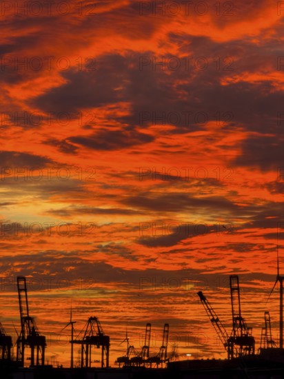 Dramatic sunset sky at Hamburg's Landungsbrücken with silhouetted cranes and wind turbines in the foreground, Hamburg, Germany