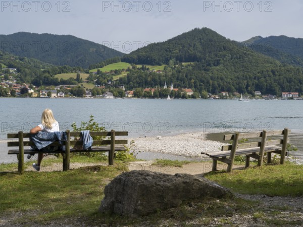 View of Tegernsee with castle, woman sitting on a bench, Bad Wiessee, Upper Bavaria, Bavaria, Germany