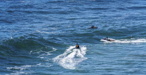 Surfers with their jet ski pilots in the Atlantic waves below Farol de Nazaré, Forte São Miguel, known as a surfer hot spot with monster waves between November and February of each year, Nazaré, Portugal