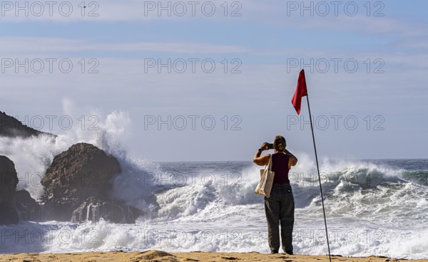 Tourists watch the waves of the Atlantic on the rocky plateau of Sito, also known as Forte São Miguel, a surfing paradise with monster waves in the months of November to February, Nazaré, Portugal