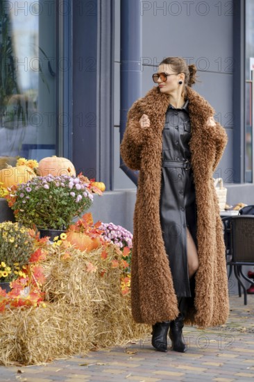 A woman stands confidently in a warm, fluffy coat at an outdoor market location surrounded by seasonal decorations
