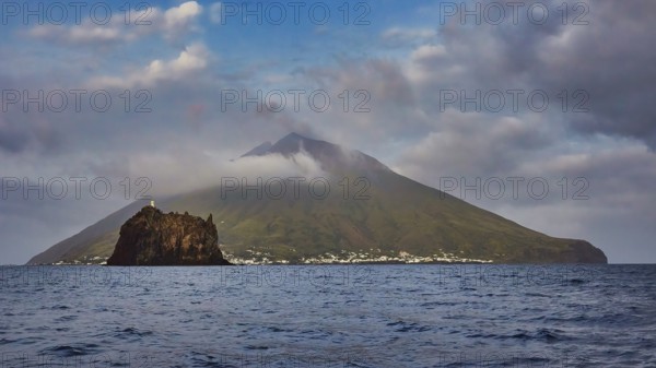 Stromboli island with offshore islet Strombolicchio, volcanic island with picturesque village surrounded by thick clouds and calm sea, UNESCO World Heritage Site, Aeolian Islands, Aeolian Islands, Sicily, Italy