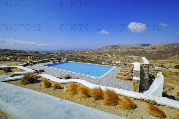 Ano Mera, Mykonos, Cyclades, Greece - Theme photo: vacation in Greece, sun loungers on the terrace of a boutique hotel with a sea view. Luxury hotel with swimming pool. Boutique Hotel Thronos Suites with views across the countryside towards the sea