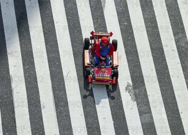 People in costumes drive small go-kart racing cars across zebra crossings, Shibuya Crossing, Shibuya, Tokyo