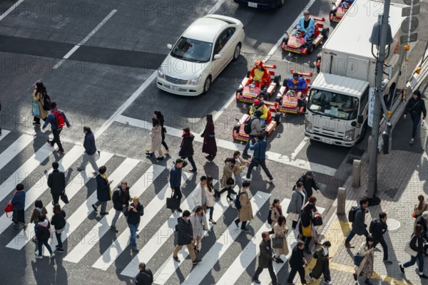 People cross zebra crossings, people in costumes ride small go-kart racing cars, Shibuya Crossing, Shibuya, Tokyo