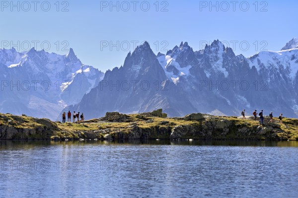 A group of hikers at Lac de Chésserys, behind the snow-covered Mont Blanc massif, Chamonix-Mont-Blanc, Haute-Savoie, France