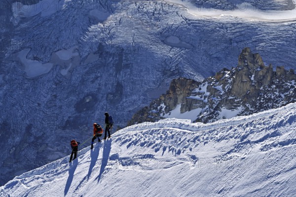Three ascended mountaineers run across a snow-covered mountain ridge, Aiguille du Midi, Chamonix-Mont-Blanc, Haute-Savoie, France
