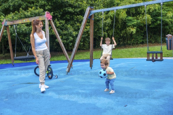 Mother enjoying a sunny day at the playground, watching her children happily playing with a ball and swinging on the swings, creating joyful moments of childhood and togetherness