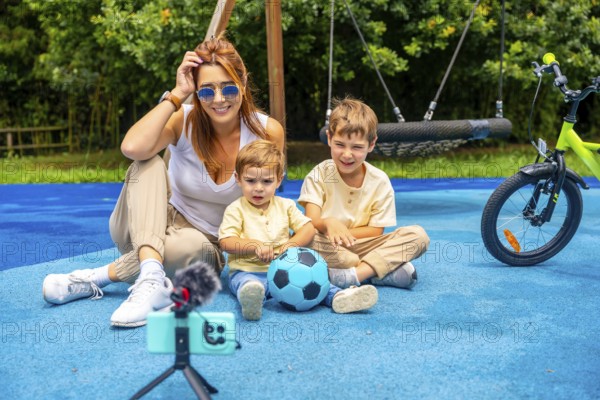 Influencer mother vlogging with her two children at the playground, capturing joyful moments with a smartphone and microphone while enjoying a sunny day filled with fun and laughter