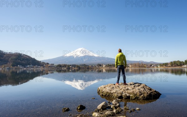 Young man standing on a rock in water, volcano Mt. Fuji is reflected in Lake Kawaguchi, Yamanashi Prefecture, Japan