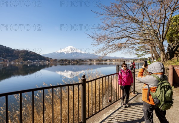 Tourists take pictures on the waterfront, Volcano Mt. Fuji is reflected in Lake Kawaguchi, Yamanashi Prefecture, Japan