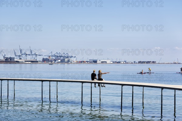 Two passers-by on circular bridge construction, wooden jetty, Infinite Bridge on Varna Beach, Ballehage Beach, architect Niels Povlsgaard, view of container port, Aarhus, Jutland, Denmark