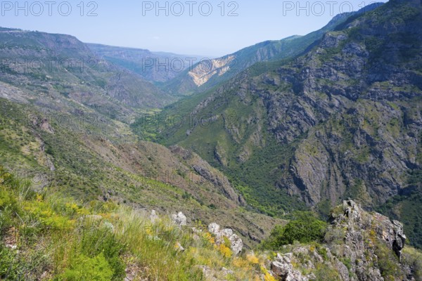 Rocky mountainside and deep valley with lush greenery under bright skies, view from the Halidzor observation deck into the Vorotan valley, Vorotan, Syunik province, Armenia