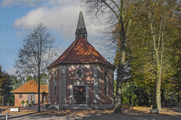 Brick chapel with pointed roof and roof turret, surrounded by autumn trees under a blue sky, Heek-Ahle, Münsterland, North Rhine-Westphalia, Germany
