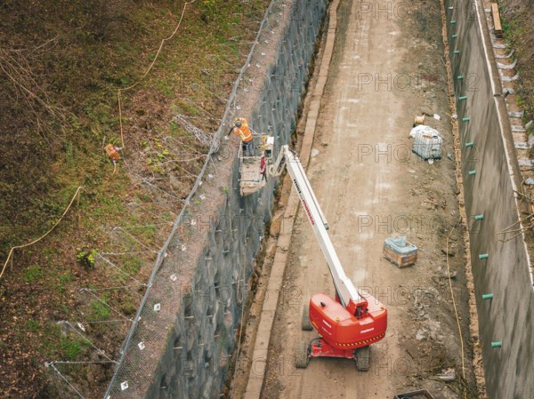 Construction workers on a lift attach a net to a steep slope, construction of the Hermann Hesse Railway, Im Hau, Calw, Germany