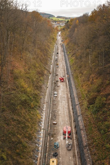 A long construction site in a wooded valley in autumn with heavy construction equipment and incipient infrastructure, construction of the Hermann Hesse Railway, Im Hau, Calw, Germany