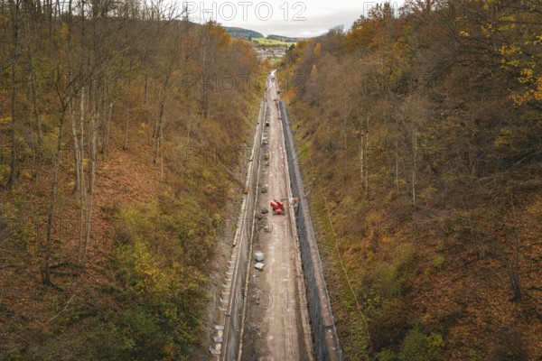 Aerial view of a construction site in an autumnal forest, with a long area of soil between steep slopes, construction of the Hermann Hesse Railway, Im Hau, Calw, Germany