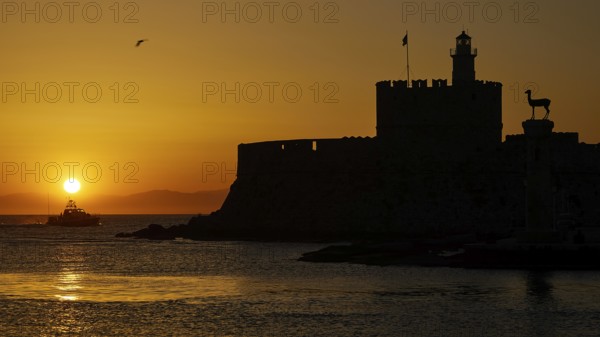 Agios Nikolaos fortress, sunrise over the sea with a castle silhouette and a passing boat, UNESCO World Heritage Site, Old Town of Rhodes Town, Rhodes, Dodecanese, Greece