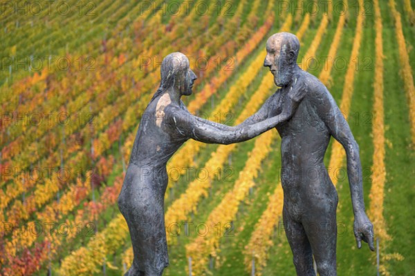 Two human figures as sculptures stand in front of colorful vines in an autumnal atmosphere, sculpture trail near Strümpfelbach im Remstal, Baden-Württemberg, Germany
