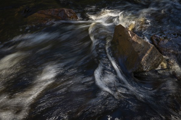 Current of a stream with dark water, reflections and turbulences, stones, long exposure, Sweden