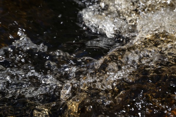 Stream flow with dark water, reflections of light and turbulence, Sweden