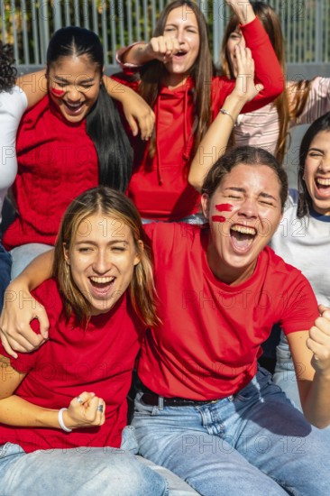 Diverse group of enthusiastic women celebrating and cheering for their favorite team at a sporting event, showing excitement, friendship, and strong fan support with red face paint